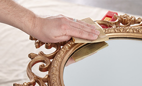 Person sanding the frame of a mirror