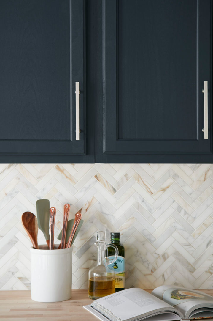 Close up of upper kitchen cabinets that are the color navy with countertop with olive oil and a container holding kitchen utensils