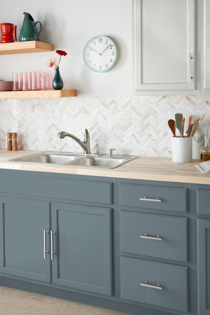 Close up of a kitchen sink with a white and grey back splash above blue cabinets
