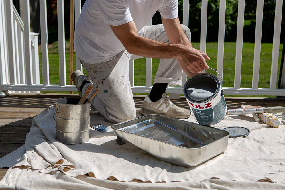 Painter pouring Kilz OverArmor Texture Slate Gray can to painting tray before painting patio deck