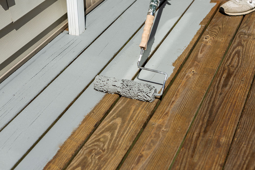  Painter applying Kilz OverArmor Texture Slate Gray with roller applicator on wood deck