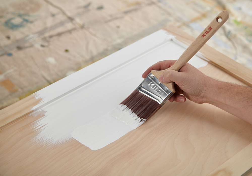 Applying primer to a cabinet door with a brush.