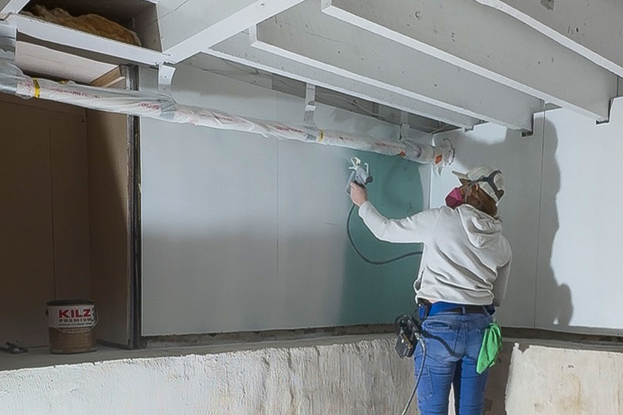Woman spraying KILZ 3® PREMIUM Interior/Exterior Primer on basement walls.